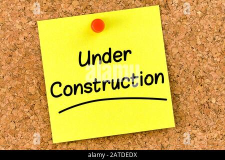 Closeup post it note on corkboard with under construction message on it Stock Photo