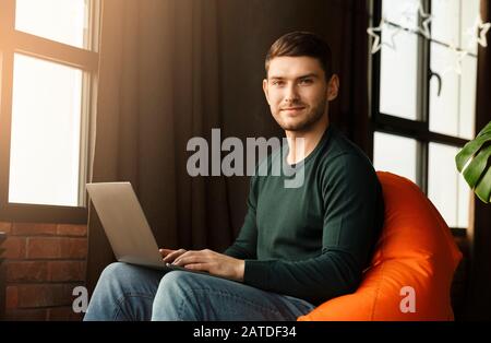 Guy Working On Laptop Looking At Camera In Coworking Workspace Stock Photo