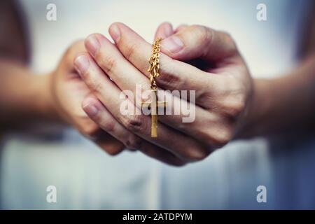 woman hands praying holding a beads rosary with Jesus Christ in the cross or Crucifix on black background. Stock Photo