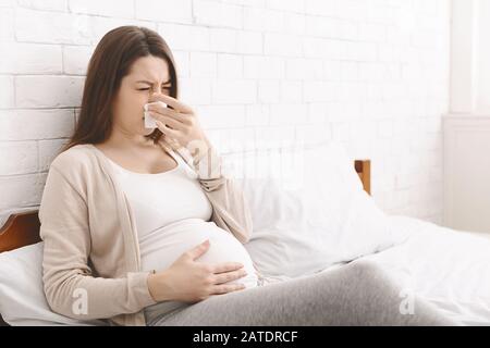 Pregnant woman suffering from snotty nose, lying in bed Stock Photo