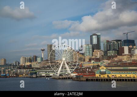 Seattle waterfront and skyline, with the Space Needle showing through the spokes of the Great Wheel ferris wheel in the foreground. Colorful image wit