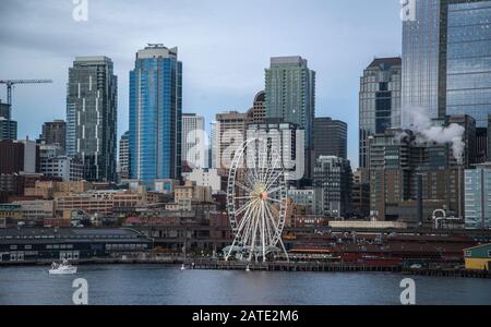 Seattle waterfront and skyline, with the Space Needle showing through the spokes of the Great Wheel ferris wheel in the foreground. Colorful image wit