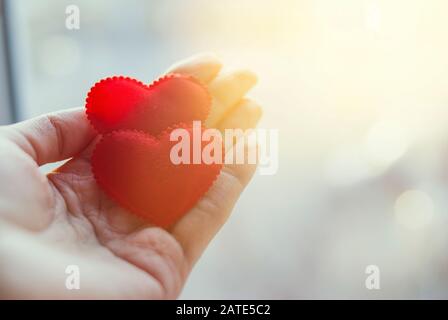 Two red hearts in a hand on a palm. Light background, sunny flare. The concept of love. Valentine's Day. Stock Photo