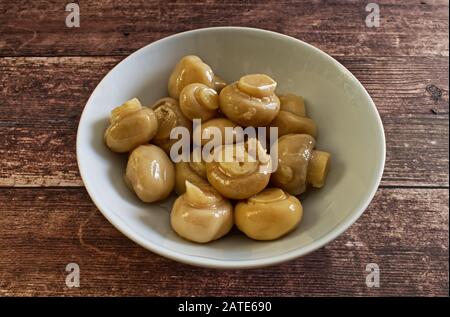 Pickled white mushrooms in white bowl on wooden table Stock Photo