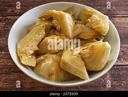 Pickled artichokes in white bowl on wooden table Stock Photo