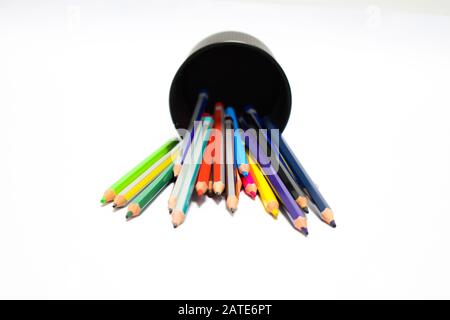 A jar full of different colored pencil crayons fallen on a white background Stock Photo