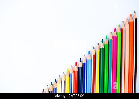 A set of different colored pencil crayons arranged from small to big on a white background Stock Photo