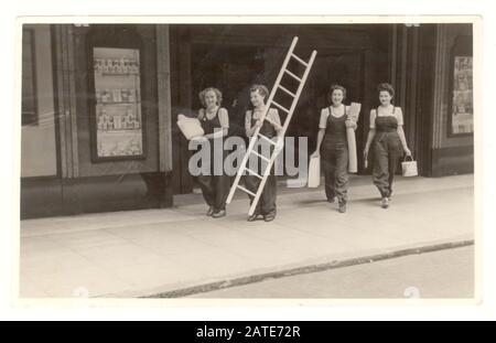 WW2 era photo of women employees, department store window dressers wearing dungarees carrying paint, fabric and a mannequin walking through the shop entrance, dated 1942, U.K. Stock Photo