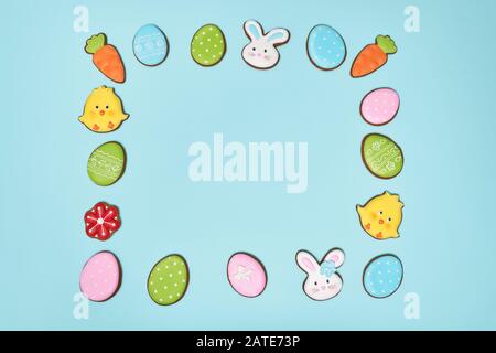 From above view of ginger glazed cookies isolated on blue. Homemade lovely delicious pastry in shape of yellow easter chicks, bunnies, carrots, flower and colorful eggs lying making square on table. Stock Photo