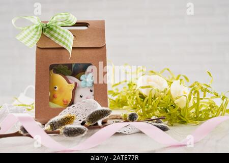 Front view of glazed cookies in shape of lovely animals, birds and eggs in brown gift box, willow branch, dried flowers and ribbons isolated on white. Selective focus of cute homemade pastry. Stock Photo