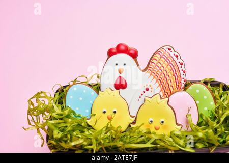 From above view of glazed cookies in shape of lovely yellow chicks, chicken and colorful eggs lying in box with fake green grass isolated on pink background. Spring and easter holidays concept. Stock Photo