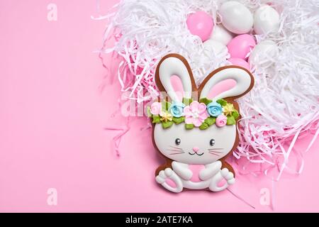 Close up of lovely pastry isolated on black background. Selective focus of easter bunny in flower wreath and eggs in white nest on pink table. Spring and Easter holiday concept. Stock Photo