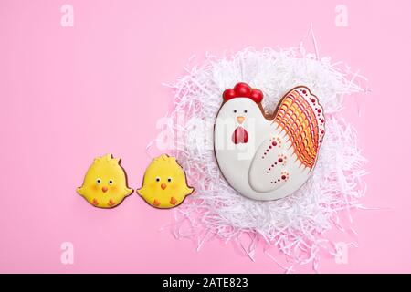 From above view of glazed cookies in shape of lovely chicken lying in white nest, two yellow chicks nearby, isolated on pink background. Close up of cute pastry. Spring and easter holidays concept. Stock Photo