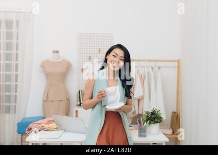 Portrait of beautiful young Asian fashion designer businesswoman at her studio while drinking coffee Stock Photo