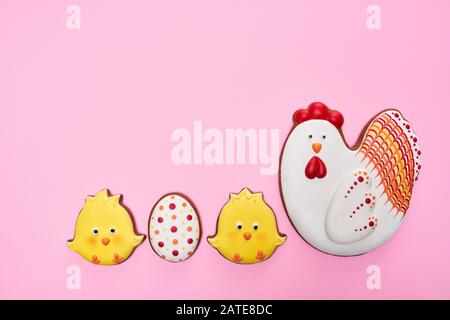 From above view of glazed cookies in shape of lovely chicken, two yellow chicks and egg, isolated on pink background. Close up of cute pastry in row. Spring and easter holidays concept. Stock Photo
