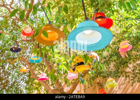 Handmade lampshades background. Cafe outside decor. Original multi-colored lampshades hanging on tree. Green tree decorated with panama lampshades. New life for old hats Closeup Stock Photo
