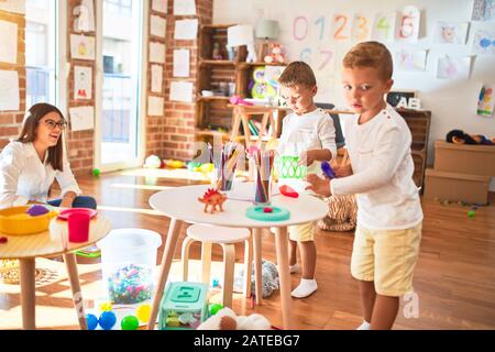 Beautiful teacher and toddlers playing cooking with plastic food around lots of toys at kindergarten Stock Photo