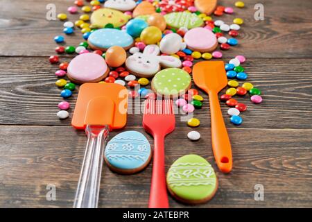 Colorful ginger glazed cookies and chocolate balls on wooden table. Homemade lovely delicious pastry in shape of easter animals, eggs and carrots, sellective focus of silicone kitchen tools nearby. Stock Photo