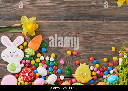 Crop of colorful ginger glazed cookies, chocolate balls and daffodils isolated on wooden background. Close up of homemade lovely delicious pastry in shape of easter animals, carrot, eggs and flowers. Stock Photo