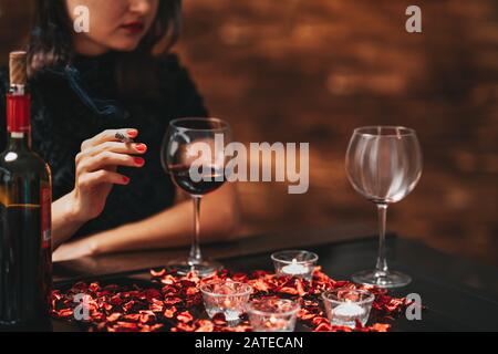 Alone and unhappy beautiful woman sitting on a table, drink wine and smoke with a bad mood Stock Photo