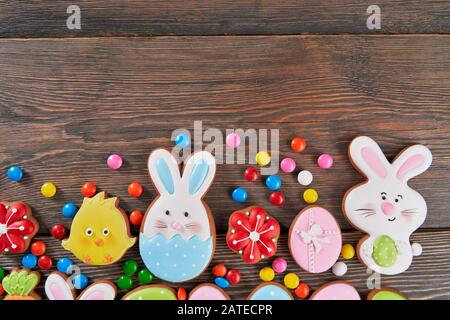 Crop of colorful ginger glazed cookies and chocolate balls isolated on wooden background. Close up of homemade lovely delicious pastry in shape of easter animals, eggs and red flowers. Stock Photo