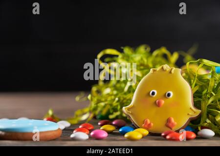 Close up of small peanut chocolate balls in crispy sugar shell isolated on black background. Selective focus of easter chick and egg near green nest on wooden table. Spring and Easter holiday concept. Stock Photo