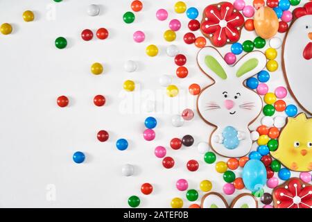 From above view of colorful ginger glazed cookies and chocolate balls isolated on white background. Close up of homemade lovely delicious pastry in shape of easter bunny holding egg and flowers. Stock Photo