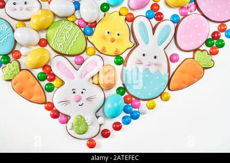 Top view of ginger glazed cookies and colorful peanut chocolate balls isolated on white background. Close up of homemade lovely delicious pastry in shape of easter animals, eggs and carrots. Stock Photo