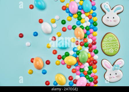 From above view of ginger glazed cookies isolated on blue background. Homemade lovely delicious pastry in shape of two easter bunnies, green egg and colorful chocolate balls in crispy sugar shell. Stock Photo