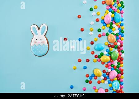 From above view of ginger glazed cookie isolated on blue background. Homemade lovely delicious pastry in shape of easter bunny in egg and colorful chocolate balls in crispy sugar shell. Stock Photo