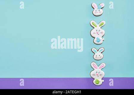 From above view of ginger glazed cookies isolated on blue and purple background. Homemade lovely delicious pastry in shape of four easter rabbits in row, two holding egg. Concept of holidays, bakery. Stock Photo
