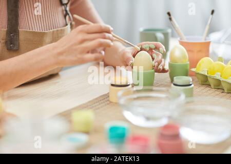 Close up of unrecognizable young woman painting eggs in pastel colors for Easter while sitting at table in kitchen or art studio, copy space Stock Photo