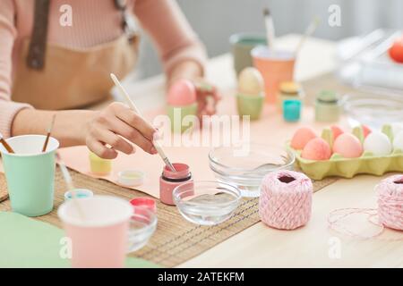 Close up of unrecognizable woman painting Easter eggs in pastel colors while sitting at table in kitchen or art studio, copy space Stock Photo