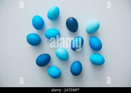 Above view of hand-painted blue Easter eggs arranged in minimal composition on white background, copy space