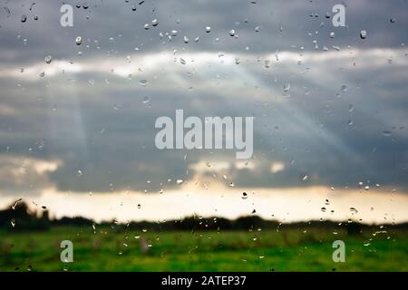 Sunbeams breaking through the clouds seen through a wet window. Stock Photo