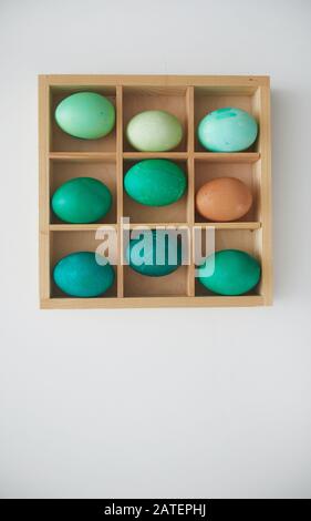 Top view of hand-painted emerald Easter eggs in wooden crate arranged in minimal composition on white background, copy space Stock Photo