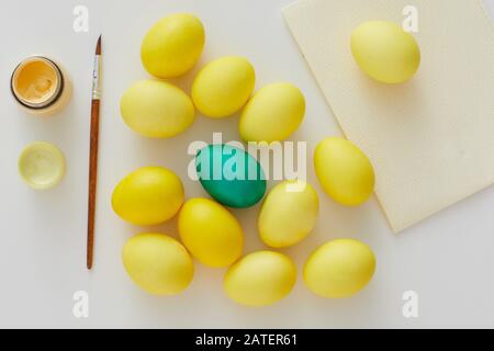 Above view of pastel yellow Easter eggs with green accent and paint brush arraigned in minimal composition on white background, copy space Stock Photo