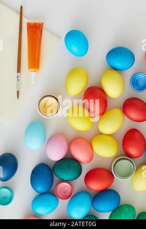 Above view of multi colored Easter eggs with paint brushes arraigned in minimal composition on white background in art studio, copy space Stock Photo