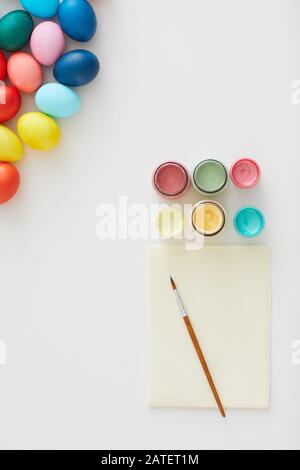 Above view of multi colored Easter eggs with paint supplies arraigned in minimal composition on white background in art studio, copy space Stock Photo