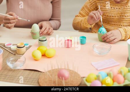 Close up of mother and daughter painting Easter eggs pastel color sitting at table in cozy kitchen interior, copy space Stock Photo