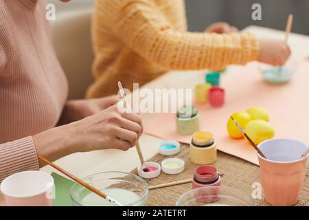 Closeup of unrecognizable mother and daughter painting Easter eggs pastel colors sitting at table in cozy kitchen interior, copy space Stock Photo