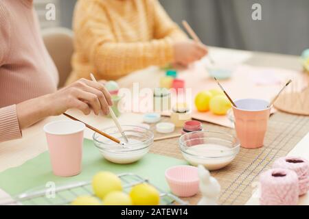Close up of unrecognizable mother and daughter painting Easter eggs pastel colors sitting at table in cozy kitchen interior, copy space Stock Photo