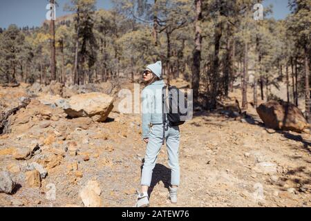 Young woman dressed casually walking with backpack in the forest highly in the mountains on the volcanic rocks, traveling on Tenerife island, Spain Stock Photo