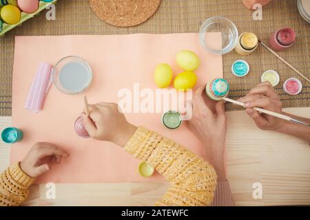 Top view close up mother and daughter painting Easter eggs pastel colors sitting at table in kitchen interior, copy space Stock Photo