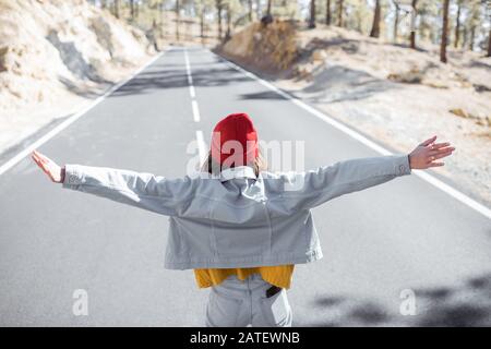 Lifestyle portrait of a stylish woman running on the beautiful mountain road, feeling happy and carefree while traveling. View from the backside Stock Photo