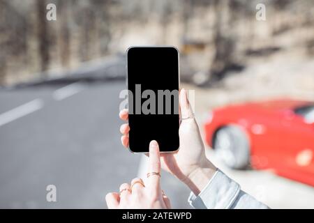 Woman holding smartphone with empty screen to copy paste on the mountain road background, close-up on phone Stock Photo