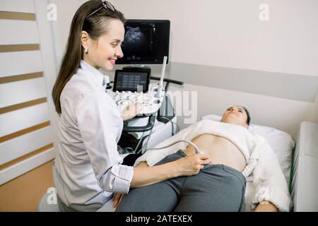 Female doctor performs ultrasound examination of pelvic organs of her female patient for diagnostic early pregnancy at the medical office. Stock Photo