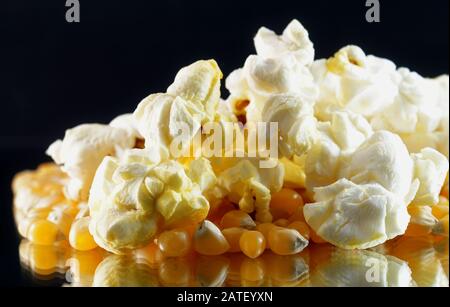 Extreme closeup of popped and unpopped seeds of popcorn on a mirror and black background Stock Photo