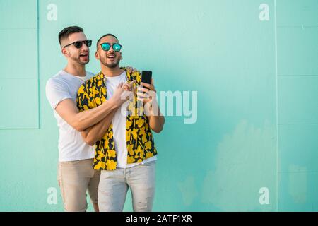 Portrait of happy gay couple spending time together and taking a selfie with mobile phone. Lgbt and love concept. Stock Photo