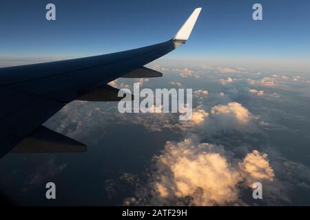 Plane wing over the Caribbean Sea clouds illuminated by setting sun Stock Photo